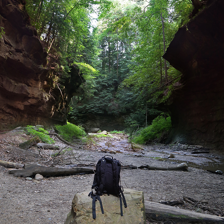 Backpack sitting on a rock, in a lush wooded canyon.