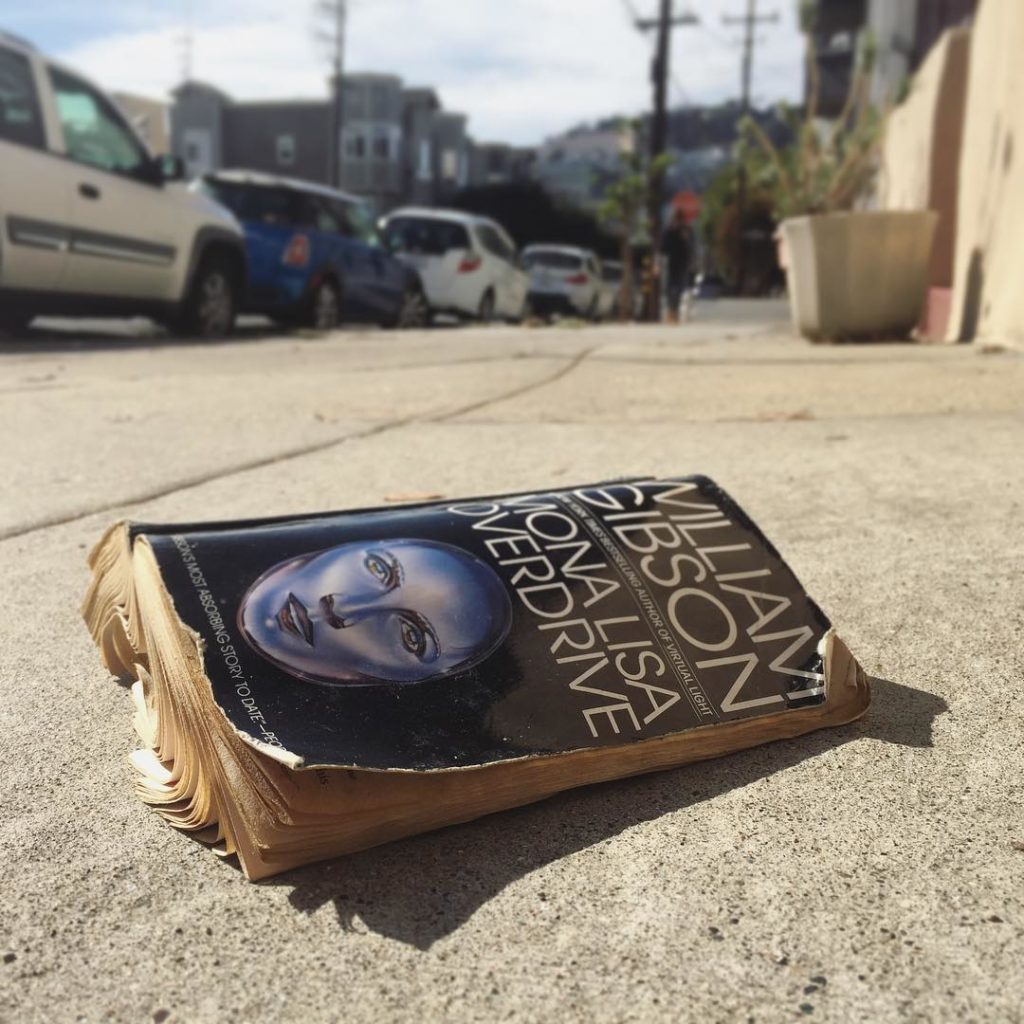 Well-worn paperback of the William Gibson novel "Mona Lisa Overdrive", lying on a San Francisco sidewalk.