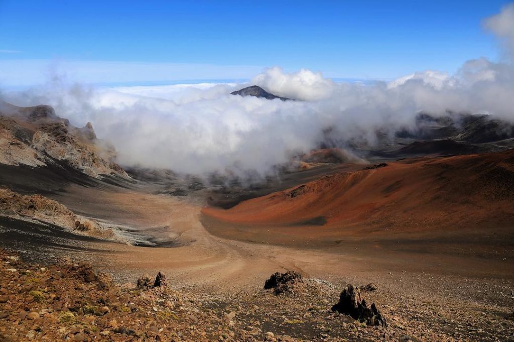 The surreal landscape of Haleakalā crater, swirled in clouds and streaks of red volcanic tufa rock.