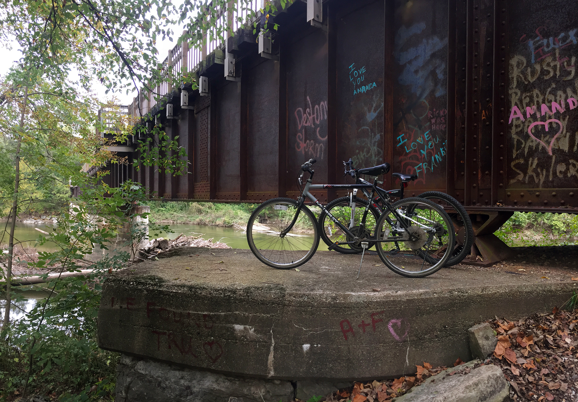 Two bikes at a trailhead beginning under a river bridge.